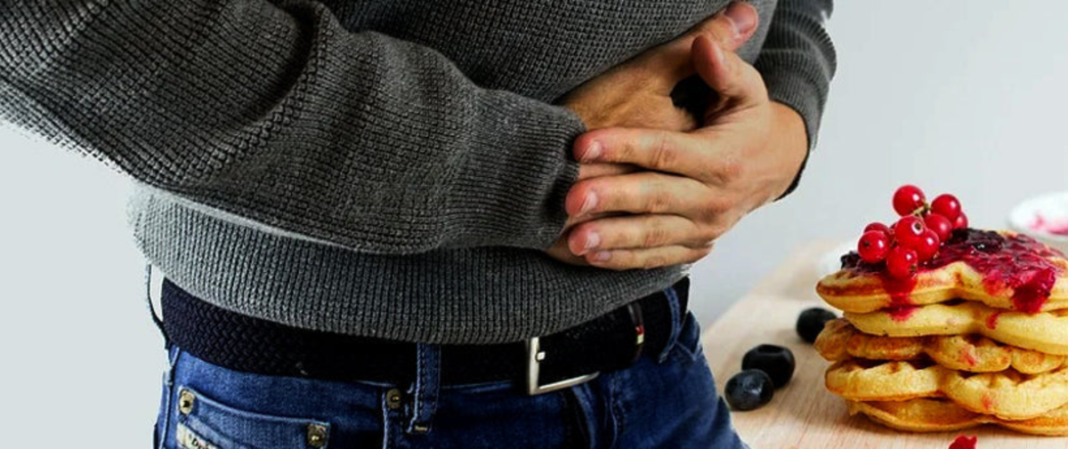 Person hält sich den Bauch vor einem Teller Pfannkuchen mit roten Beeren – Hunger als Diät-Feind