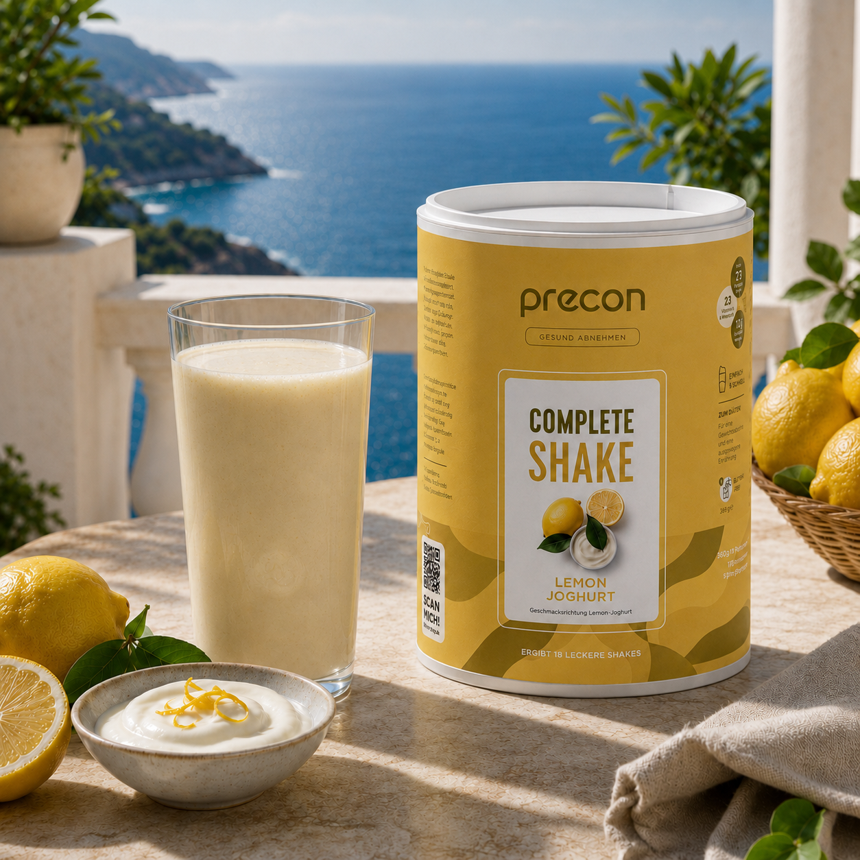 Auf einem Tisch mit Blick auf das Meer stehen in strahlendem Sonnenlicht eine Packung „Complete Shake Lemon-Joghurt“-Pulver der Anona GmbH, ein Glas des zubereiteten Shakes, eine Schüssel Joghurt mit Zitronenschale sowie frische Zitronen.